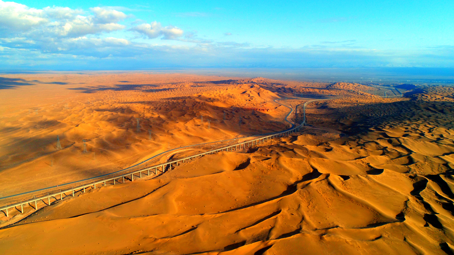 沙山沟特大桥位于甘肃省酒泉市阿克塞哈萨克族自治县境内的库姆塔格沙漠内，是一座穿越活动性沙漠地区的特长桥梁。建设者首创移动沙丘地区旋挖钻钢护筒跟进干法成孔施工工法，有效解决了流沙地质极易坍孔、成孔困难的技术难题，填补了国内空白。图为全长10.6公里的沙山沟特大桥穿越戈壁沙漠。（金伟 摄）