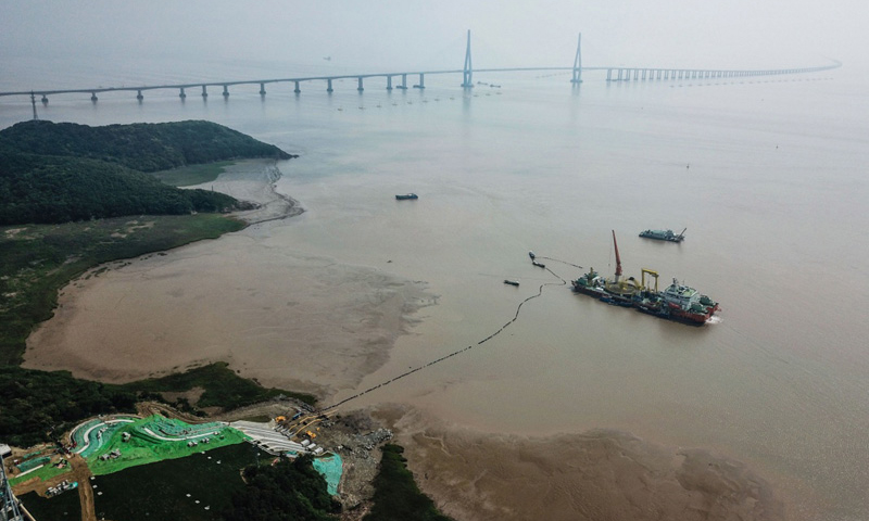 图为6月2日，最后一段海底电缆从海缆施工船上缓缓拖向舟山大鹏山岛的终端站，远处是舟山跨海大桥。（新华社记者 徐昱 摄）