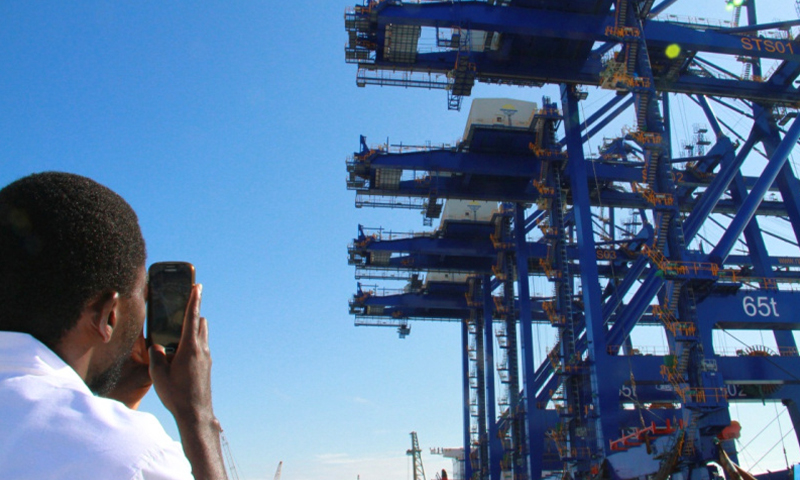 2月9日，在纳米比亚沃尔维斯湾正在建设的集装箱码头，一名男子给运载着四台岸桥的货轮拍照。（新华社记者 吴长伟 摄）