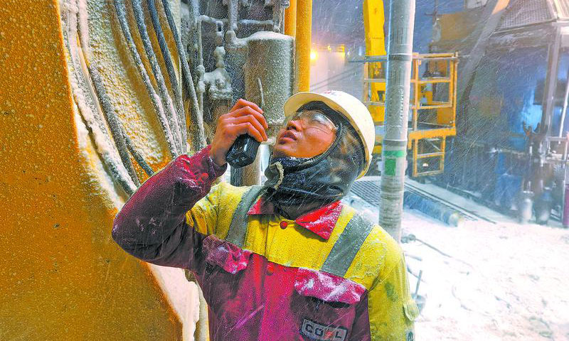11月7日凌晨，渤海辽东湾迎来2021年冬季第一场暴风雪，气温骤降至零下2℃，最大风力达10级以上，对海上一线生产带来极大挑战。图为暴风雪导致钻台视线不佳，副司钻手持对讲机辅助司钻操作排管机抓取钻具。