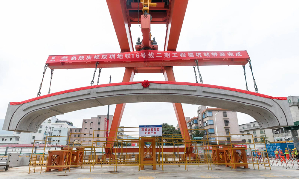 据介绍，福坑站处于岩溶发育区，最大一处溶洞体积近4000立方米，地质条件差，对拼装时的围护结构变形控制带来了巨大的挑战。该项目大力推进“智能化+信息化+数字化”智能制造平台建设，通过BIM模型可视化系统等技术应用，实现了集勘察、测量、施工、注浆等于一体的全方位智能化管理。项目组还自主研发了具备旋转、防摇摆、姿态微调、纠偏等多功能“180吨门式起重机+分离式拼装台车”工装设备，实现了梁、板、柱、墙等预制构件的吊装、翻转、旋转等姿态调整，达到了毫米级的精准拼装。图为最后一块顶板吊装。