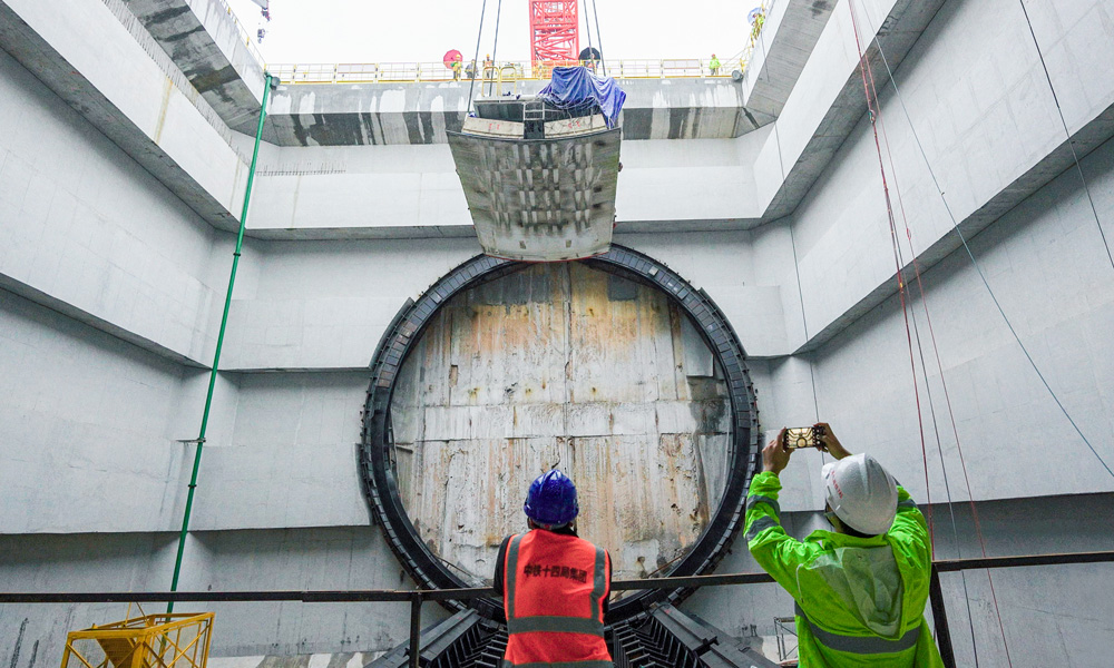 为隧道建设量身定制的盾构机“英雄号”全长134米，开挖直径14.8米。连日来，盾构机主驱动、刀盘、拼装机等已运输下井、完成组装，后期将进行盾构机管线连接和整机调试工作，即将开始盾构隧道掘进。图为施工人员在现场紧盯盾体下井定位组装。