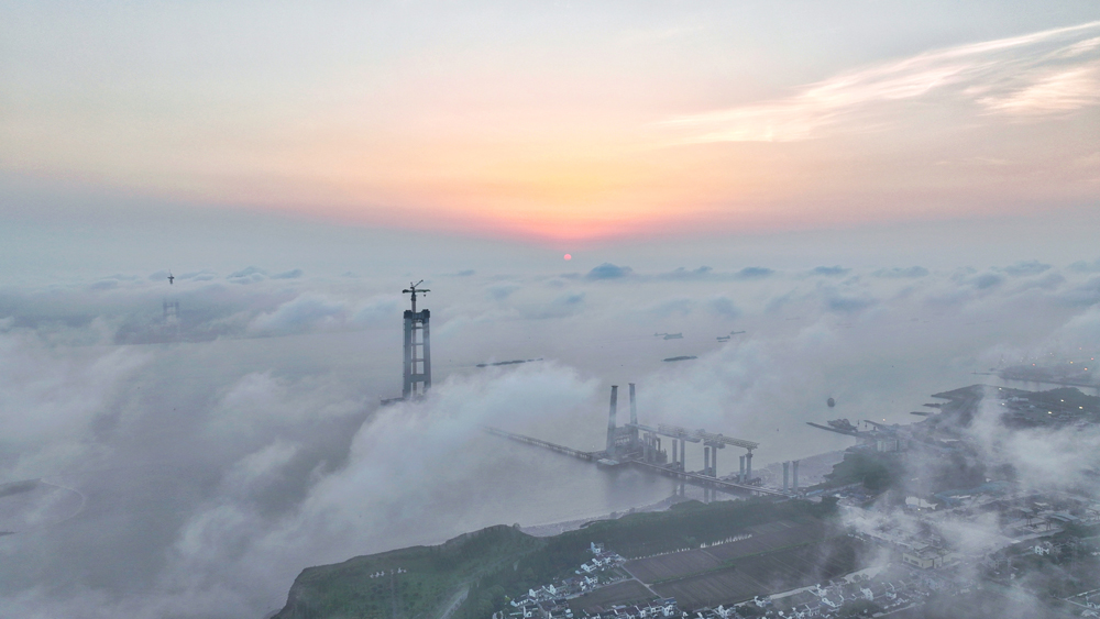 清晨，建设中的江苏张靖皋长江大桥雨后初霁，旭日照亮云层，大桥雏形若隐若现，美轮美奂。目前，中国交建旗下中交二航局承建的张靖皋长江大桥南主塔建设高度已达220多米，预计2025年底可实现封顶，届时高度将达350米，为世界最高悬索桥索塔。