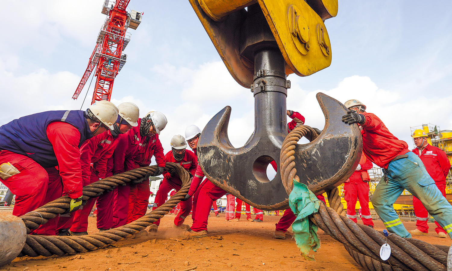 在中国海油海油工程制造场地，施工人员合力将大直径钢丝绳挂扣在吊钩上。