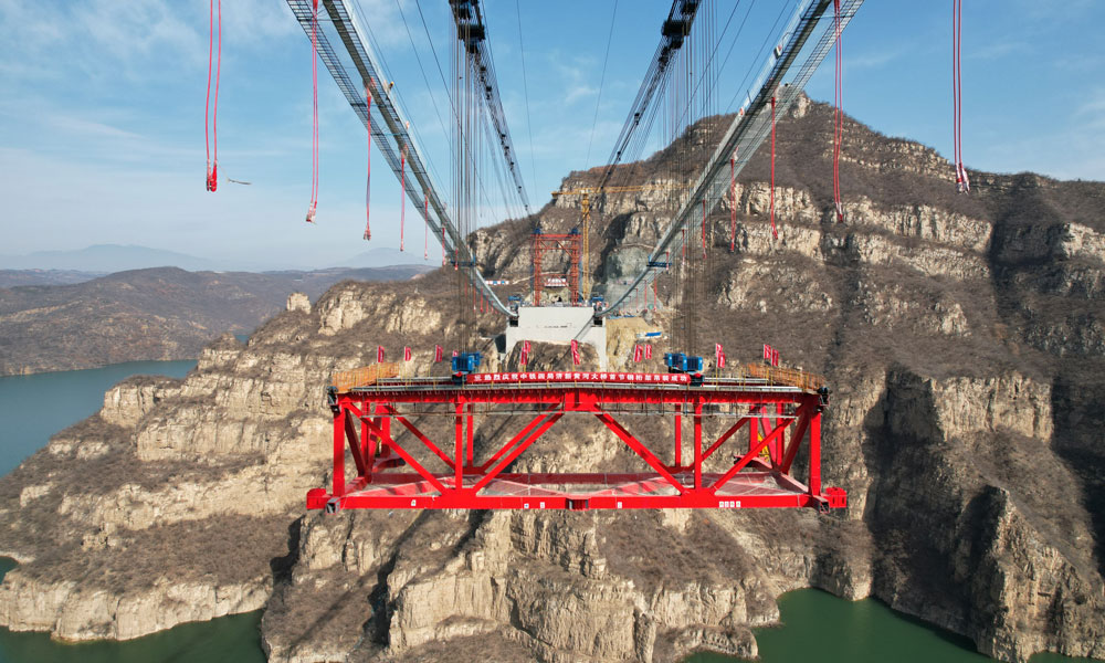 2月14日，中铁四局承建的济新高速公路黄河大桥首节钢桁梁吊装，标志着世界最大跨度回转缆悬索桥正式进入桥面安装阶段，为实现2025年底全线建成通车目标奠定坚实基础。济新黄河大桥位于河南省济源市与新安县交界的王屋山-黛眉山世界地质公园内，横跨黄河小浪底库区，主跨555米，塔高109米，采用双向六车道高速公路标准建造。本次吊装的首节钢桁梁长17.9米，桁高7.5米，桥面宽37.4米，重约260吨。全桥由34节钢桁梁组成，总重约10200吨。