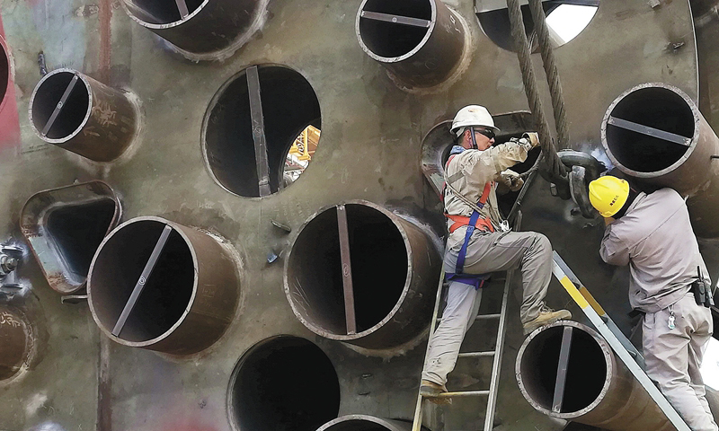 5月15日，海西湾畔，中国海油所属海洋石油工程股份有限公司青岛场地码头，一座身着崭新红蓝外衣的“钢铁巨城”静静漂浮在轻雾缭绕的海面上。图为作业人员安装吊装锁具。