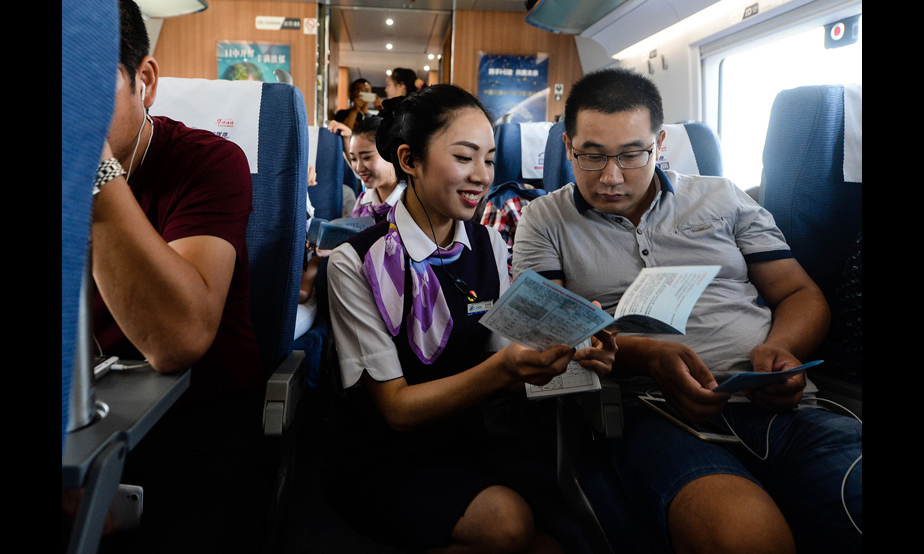 2016年9月10日，在上海虹桥站开往郑州东站的G1802次列车上，乘务员夏梦雅给乘客发放宣传资料，讲解注意事项（季春鹏 摄）。