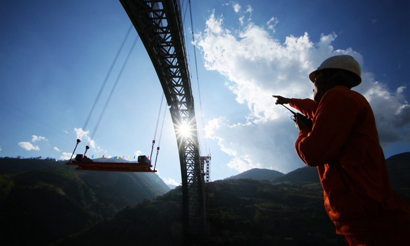 怒江四线特大桥主跨为单跨达490米的钢桁拱，一跨飞越怒江天堑，是目前世界上铁路拱桥的最大跨度。图为中铁十八局技术人员指挥怒江四线特大桥钢杆件吊装。（新华社发）